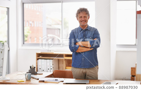 Finally, I have an office with a window. Portrait of a mature businessman standing with his arms folded behind his desk. 88987030