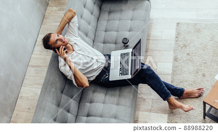 young man is talking on a smartphone in his living room . young man is talking on a smartphone in his living room . 88988220