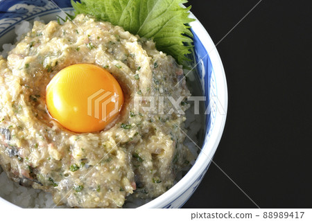 A bird's-eye view of a horse mackerel namero bowl topped with egg yolk on a black background 88989417