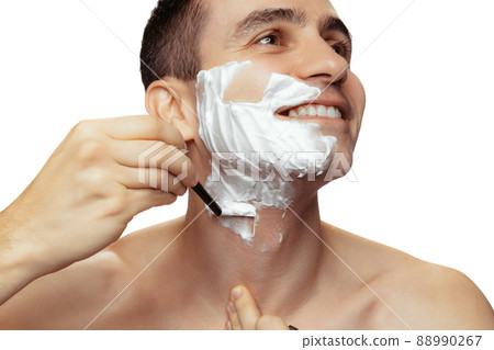 Portrait of young smiling man with shaving face with cream and razor isolated over white studio background. Smooth skin 88990267