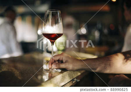 Man holding a glass of red wine in a restaurant or cafe on a wooden table in front of the window 88990825