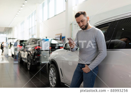 a man studies the offer of insurance companies in a car dealership on a smartphone 88993256