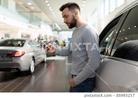 a man on the phone studies the features of an SUV in a car dealership a man on the phone studies the features of an SUV in a car dealership 88993257