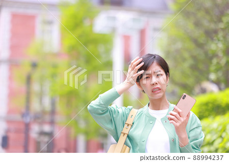 A woman holding a smartphone and holding her head looking at the camera 1 A woman holding a smartphone and holding her head looking at the camera 1 88994237