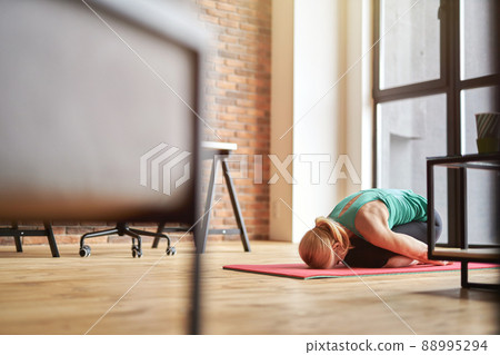 Mature blonde woman practicing yoga at home, sitting in Child pose, Balasana on the floor in modern apartment Mature blonde woman practicing yoga at home, sitting in Child pose, Balasana on the floor in modern apartment 88995294