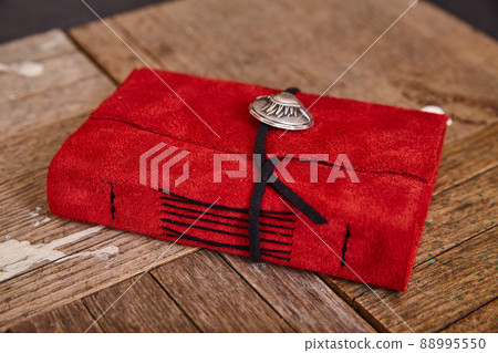 Detail of closed red leather journal with black thread on wood background Detail of closed red leather journal with black thread on wood background 88995550