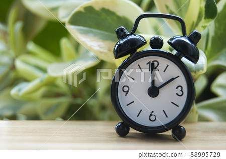 Black alarm clock isolated on blurred nature background. The clock set at 2 o'clock. Copy space concept 88995729
