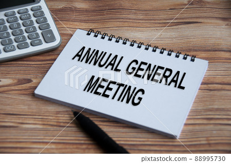 Annual general meeting text on notepad with calculator, pen and wooden table background. 88995730
