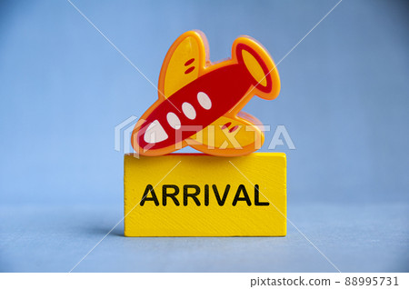 Arrival text on yellow wooden block with toy plane on top. Travelling and vacation concept 88995731