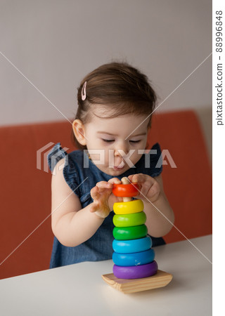 Baby girl playing with wooden colourful toy pyramid at home. 88996848