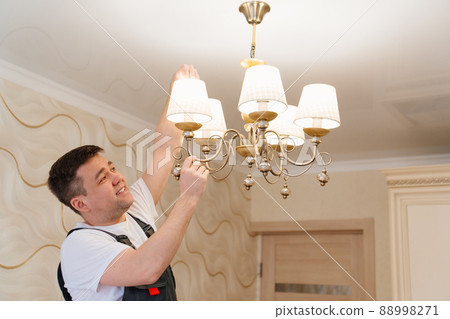 A male electrician changes the light bulbs in the ceiling light. A male electrician changes the light bulbs in the ceiling light. 88998271