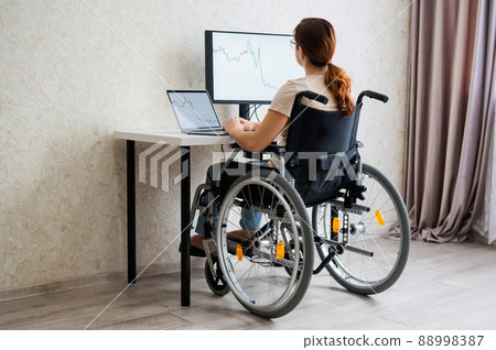 Caucasian woman in a wheelchair typing with a laptop from home. Remote work for people with disabilities. Caucasian woman in a wheelchair typing with a laptop from home. Remote work for people with disabilities. 88998387