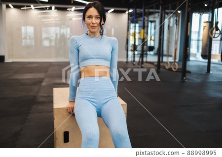 Woman in blue sportswear doing triceps exercises on wooden crossfit jump box at gym 88998995