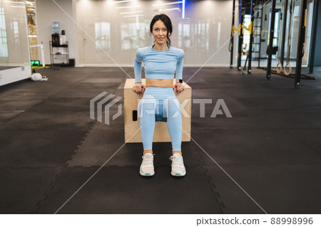Fitness woman in blue sportswear doing triceps exercises on wooden crossfit jump box at gym 88998996
