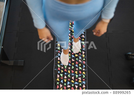 Acupuncture points of the foot stimulation. Woman stand on orthopedic foot massage mat. Massage rug with colorful stones Acupuncture points of the foot stimulation. Woman stand on orthopedic foot massage mat. Massage rug with colorful stones 88999265