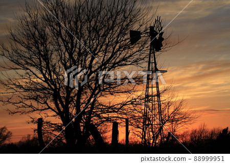 Kansas colorful Sunset with clouds, trees, and a Windmill silhouette north of Hutchinson Kansas USA. Kansas colorful Sunset with clouds, trees, and a Windmill silhouette north of Hutchinson Kansas USA. 88999951