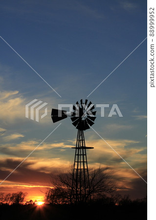 Kansas colorful Sunset with clouds, trees, and a Windmill silhouette north of Hutchinson Kansas USA. Kansas colorful Sunset with clouds, trees, and a Windmill silhouette north of Hutchinson Kansas USA. 88999952