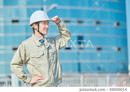 一個穿著工作服的年輕人戴著頭盔站在大樓前 89000014