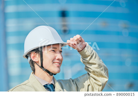 一個穿著工作服的年輕人戴著頭盔站在大樓前 一個穿著工作服的年輕人戴著頭盔站在大樓前 89000015