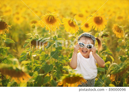 A little cute funny girl in sunglasses laughs in a huge field of sunflowers at sunset. A little cute funny girl in sunglasses laughs in a huge field of sunflowers at sunset. 89000096
