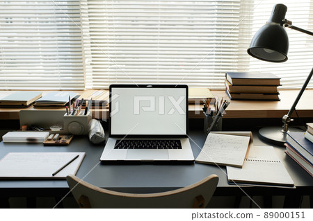 Laptop with blank screen, notepads, supplies in organizers and lamp on students table against window closed with blinds Laptop with blank screen, notepads, supplies in organizers and lamp on students table against window closed with blinds 89000151