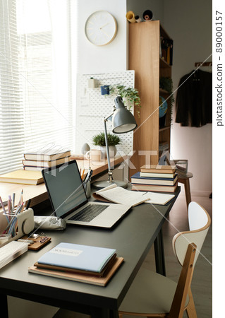 Modern workplace of student consisting of electric lamp, books, sketchpad, laptop and office supplies against window with blinds 89000157