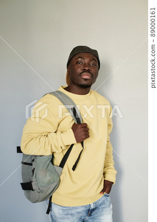 Portrait of serious handsome Black student guy in yellow sweatshirt and cap standing with satchel against isolated baclground Portrait of serious handsome Black student guy in yellow sweatshirt and cap standing with satchel against isolated baclground 89000161