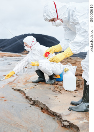 Environmental scientists in protective suits and respirators putting samples into containers whilr researching contaminated samples in toxic area 89000616