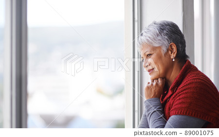 Lost in thought. Shot of a mature woman standing by a window on a sunny day. Lost in thought. Shot of a mature woman standing by a window on a sunny day. 89001075