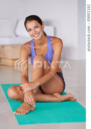 Keeping a positive attitude is half the work. Portrait of a beautiful young woman sitting on a yoga mat at home. 89001162