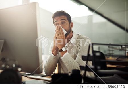 Could this be the flu coming on. Shot of a handsome young businessman blowing his nose while working late in an office. 89001420