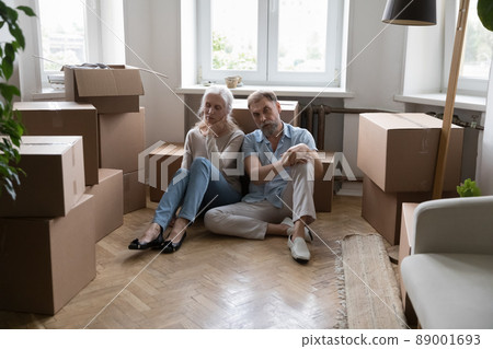 Tired elderly couple sit on floor near boxes with belongings 89001693