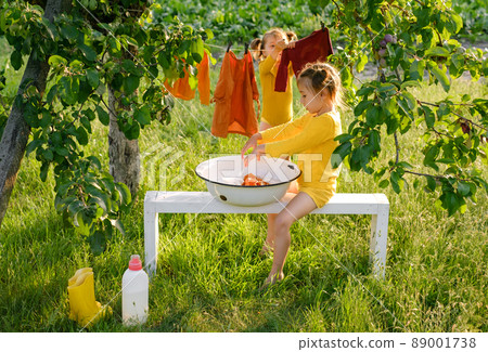 Children help their mother with the housework, washing clothes and hanging them on a clothesline in the garden outdoors. Kids have fun doing laundry together. Detergent for washing baby stuff 89001738