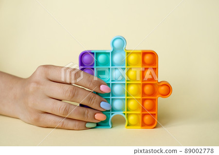 In the female hand, the popular popit toy. Anti-stress toy. entertaining games for children and adults. simple dimple. Women's nails of different colors. Colorful summer manicure. 89002778