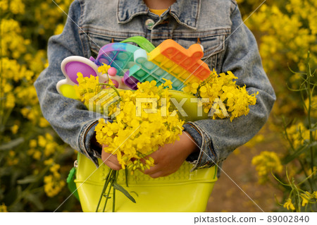 A girl in a rapeseed field with a backpack filled with modern educational popit and simple dimple toys. A bouquet of rapeseed flowers in the hands of a child. Toys made of plastic 89002840