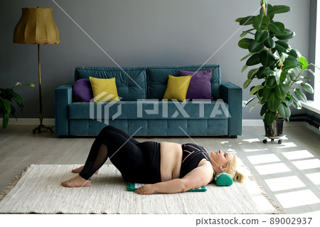 An overweight woman is lying on the floor on a massage mat with a needle pillow. Alternative treatment of back and neck pain as a consequence of obesity. Relaxing independent home massage. An overweight woman is lying on the floor on a massage mat with a needle pillow. Alternative treatment of back and neck pain as a consequence of obesity. Relaxing independent home massage. 89002937