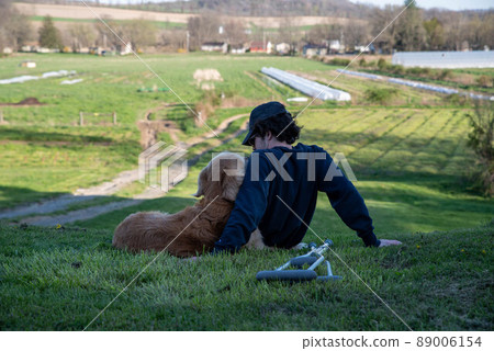 Young man cuddles old Golden Retriever on a hill with crutches on ground Young man cuddles old Golden Retriever on a hill with crutches on ground 89006154