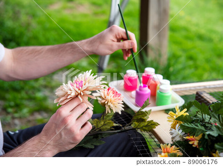 Closeup of a male artist's hands painting silk flowers outdoors Closeup of a male artist's hands painting silk flowers outdoors 89006176