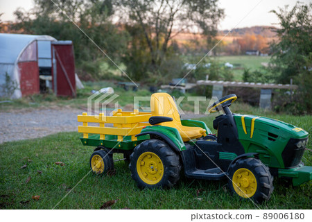 Green and yellow child's toy riding tractor in green grass yard farm background 89006180