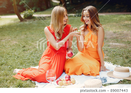 Beautiful girl in a red dress. Women sitting in a summer park. 89007443