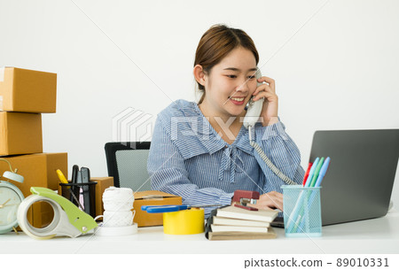 Young Asian woman business owner with many parcel boxes on the table happy online sales job, use the laptop, get an order from customers, take notes, and make arrangements for delivery by post Young Asian woman business owner with many parcel boxes on the table happy online sales job, use the laptop, get an order from customers, take notes, and make arrangements for delivery by post 89010331