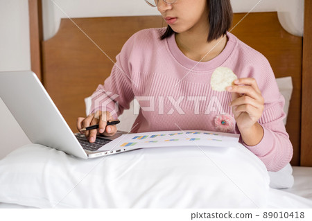work from home, a young Asian woman who works in finance at home calculates financial graphs showing the results of his investments, planning the steps of his business growth work from home, a young Asian woman who works in finance at home calculates financial graphs showing the results of his investments, planning the steps of his business growth 89010418