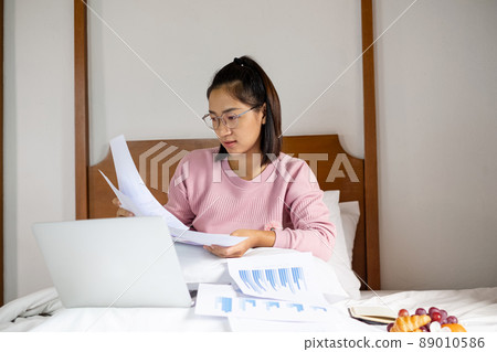 work from home, a young Asian woman who works in finance at home calculates financial graphs showing the results of his investments, planning the steps of his business growth work from home, a young Asian woman who works in finance at home calculates financial graphs showing the results of his investments, planning the steps of his business growth 89010586
