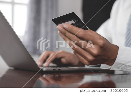The businessman's hand is holding a credit card and using a laptop for online shopping and internet payment 89010605