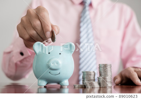 The hand of a businessman puts coins in a piggy bank, saves money with coins, steps into a successful growth business, and saves for retirement concept The hand of a businessman puts coins in a piggy bank, saves money with coins, steps into a successful growth business, and saves for retirement concept 89010623