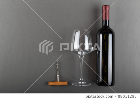 Corked red wine bottle, corkscrew and empty wine glass on gray background. Alcoholic drink.  89011283