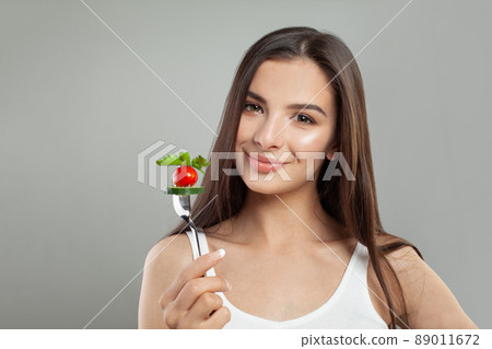 Portrait of attractive young smiling woman eating vegetable salad and holding fork in hand  89011672