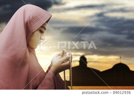 Asian Muslim woman in veil praying with prayer beads on her hands Asian Muslim woman in veil praying with prayer beads on her hands 89012936