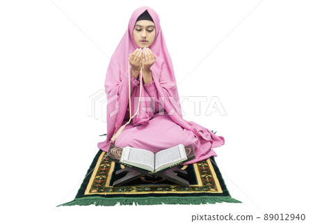 Asian Muslim woman in a veil sitting while raised hands and praying with prayer beads 89012940