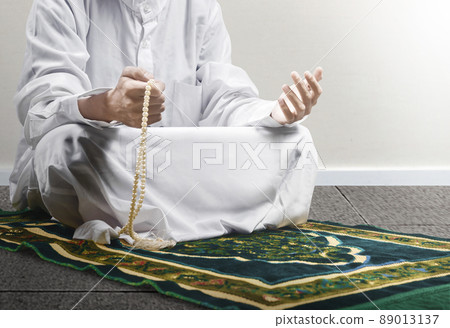 Muslim man praying with prayer beads on his hands while sitting on the prayer rug 89013137